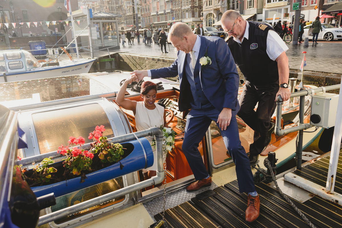 groom helping bride disembark from canal boat in Damrak after gemmente wedding ceremony in amsterdam