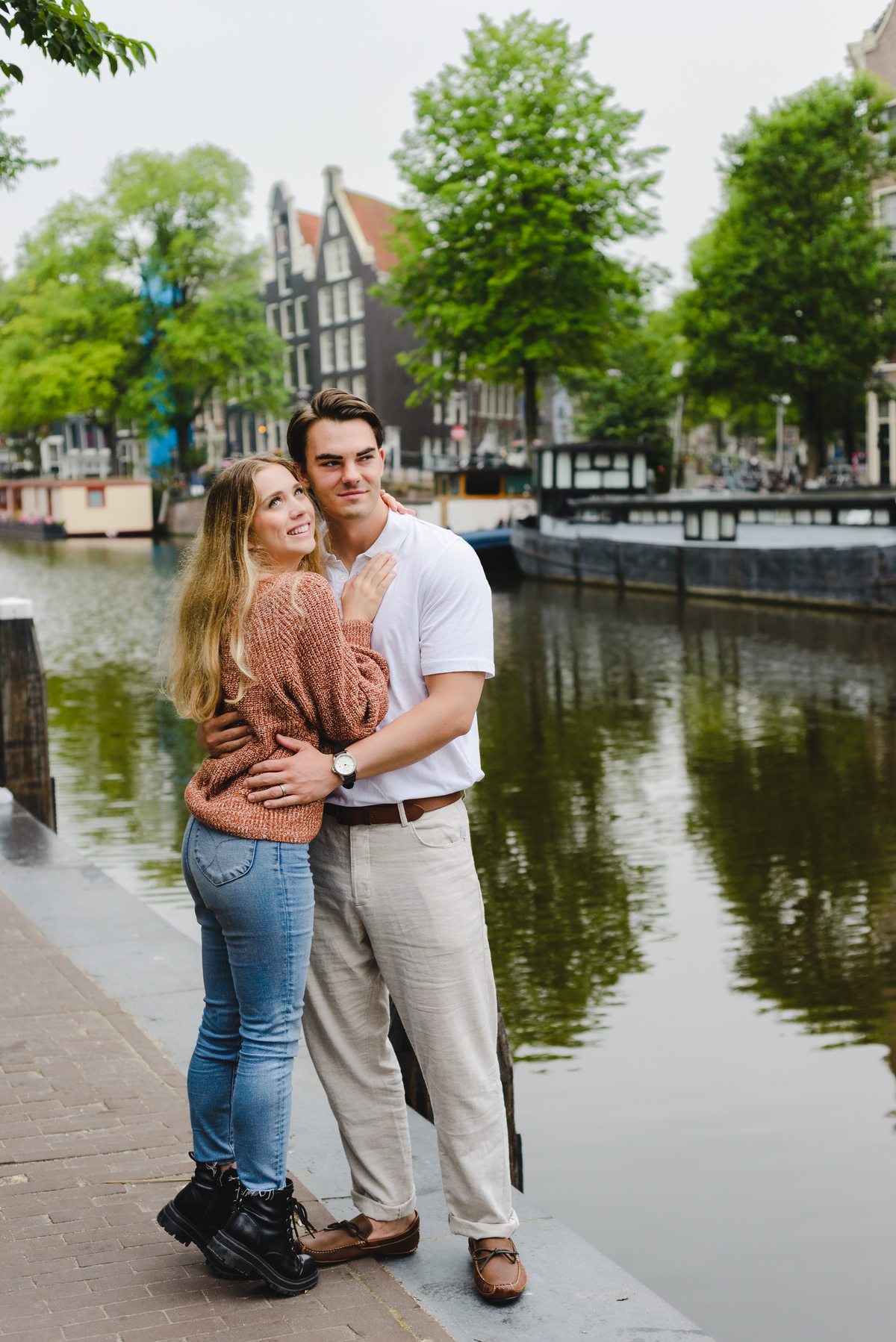 Romantic couple portrait with canal reflections and historic Amsterdam buildings.