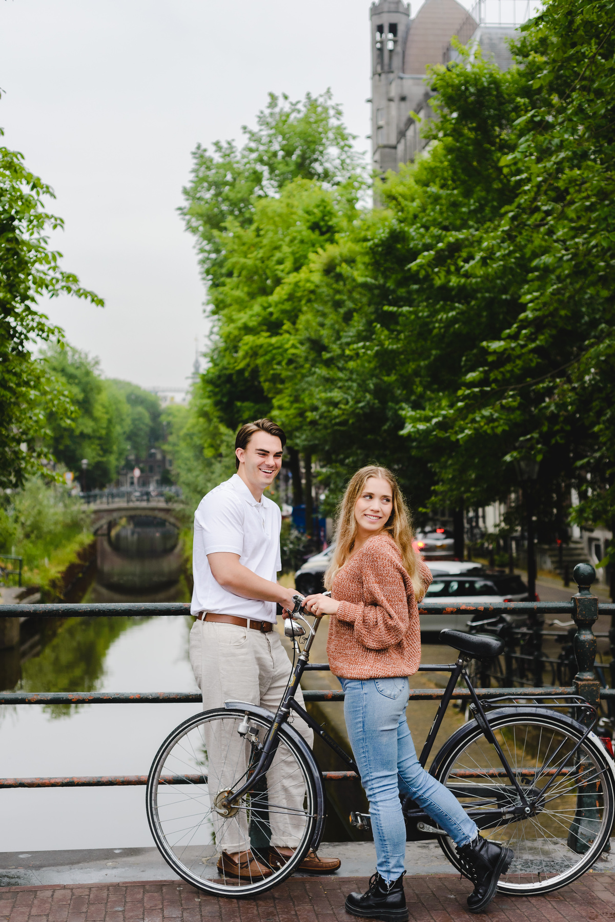 couple posing casually with a bicycle on a bridge in Amsterdam.