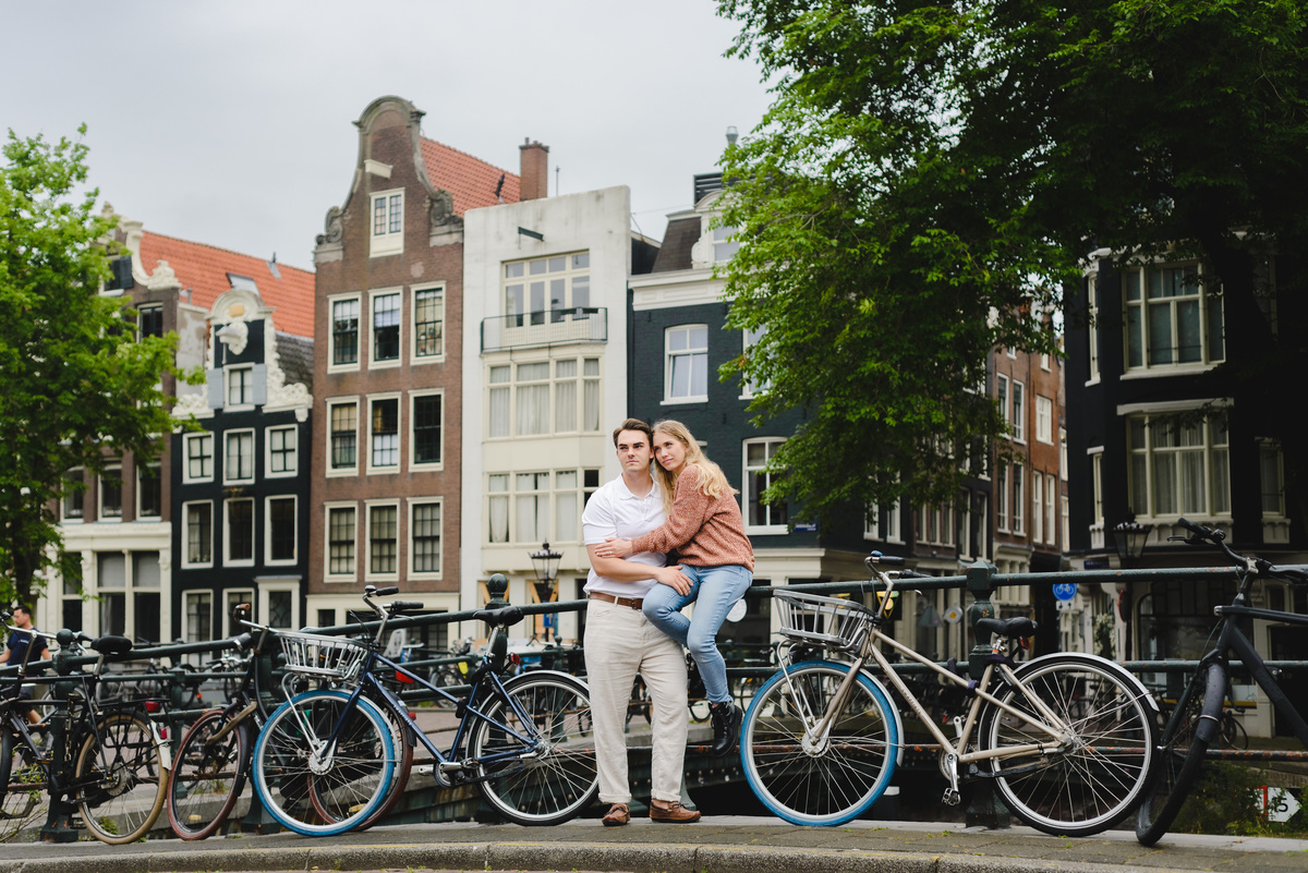 Wide angle portrait of a couple framed by Amsterdam canal houses and water below.