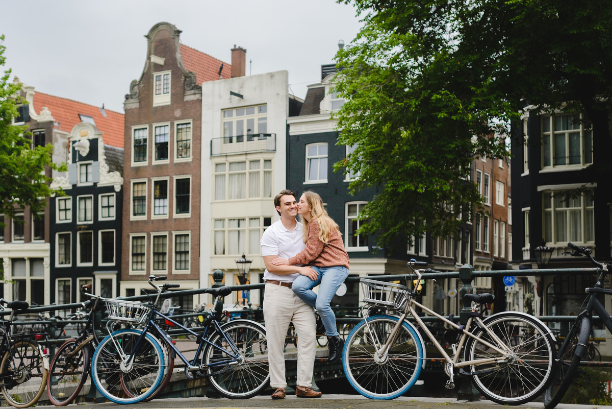 Wide angle portrait of a couple framed by Amsterdam canal houses and water below.
