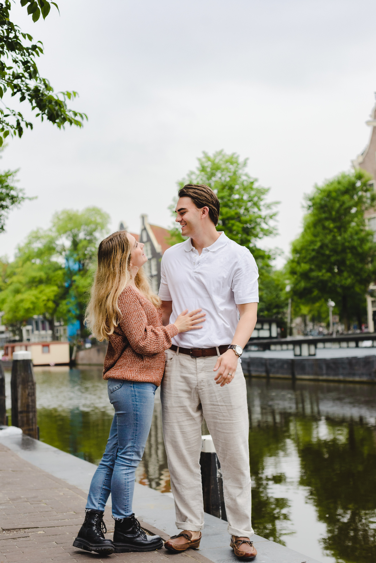 Romantic couple portrait with canal reflections and historic Amsterdam buildings.