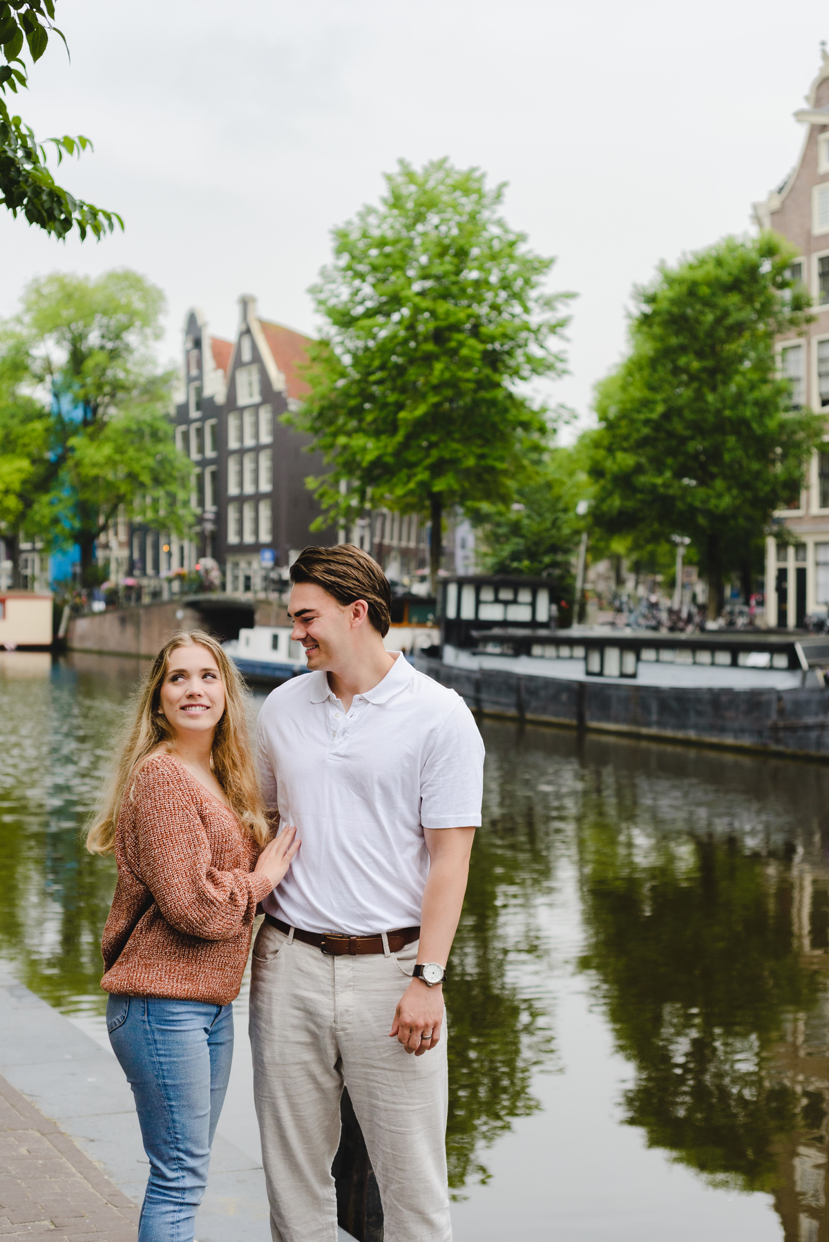 Romantic couple portrait with canal reflections and historic Amsterdam buildings.