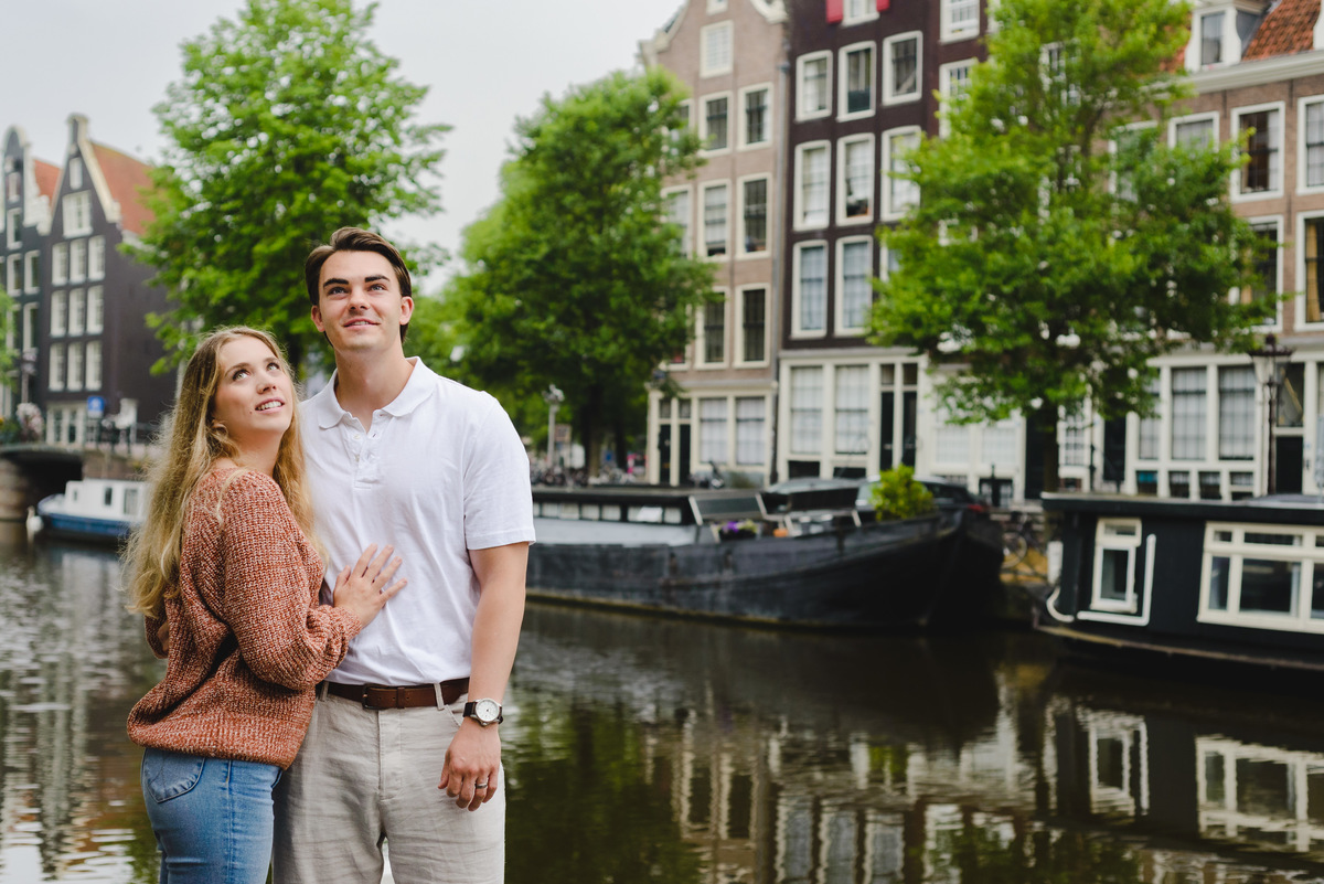 Romantic couple portrait with canal reflections and historic Amsterdam buildings.