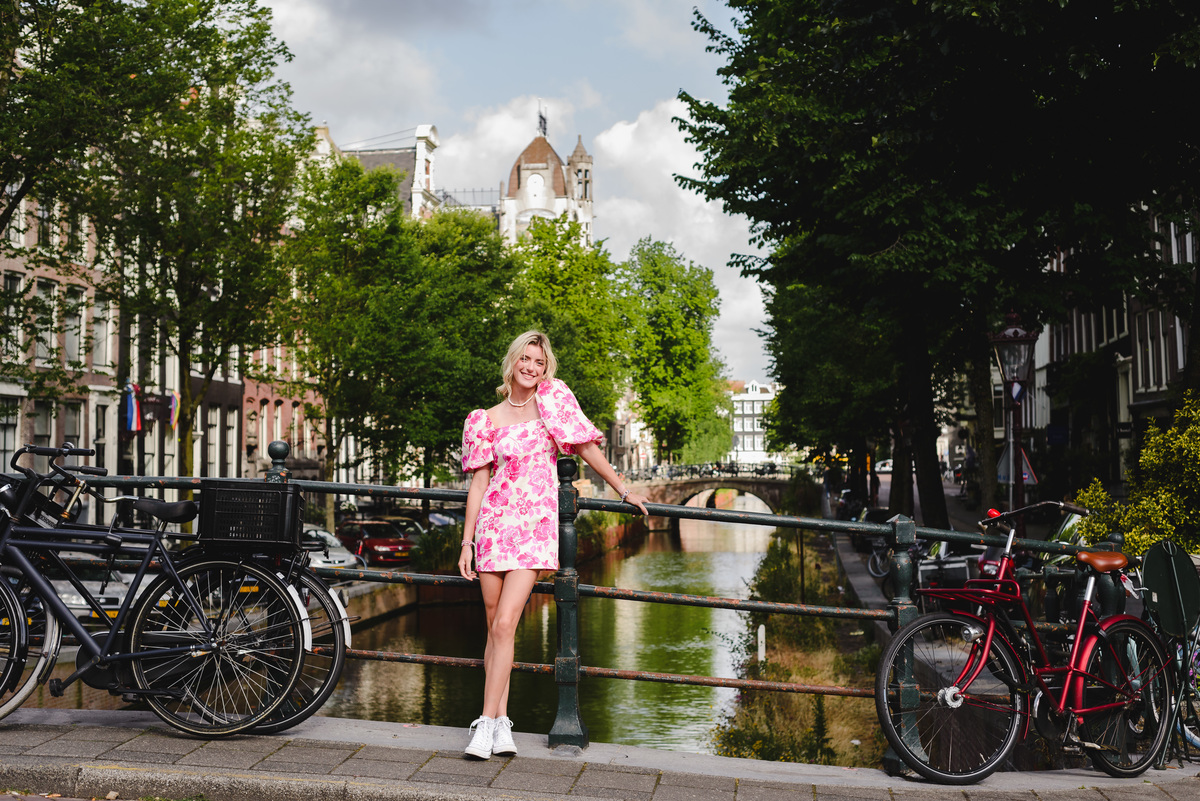 Teenage girl standing by an Amsterdam canal with historic buildings and summer greenery