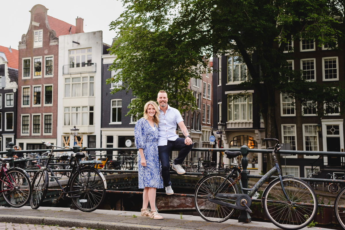 Couple standing by an Amsterdam canal with bicycles and historic Dutch architecture in the background
