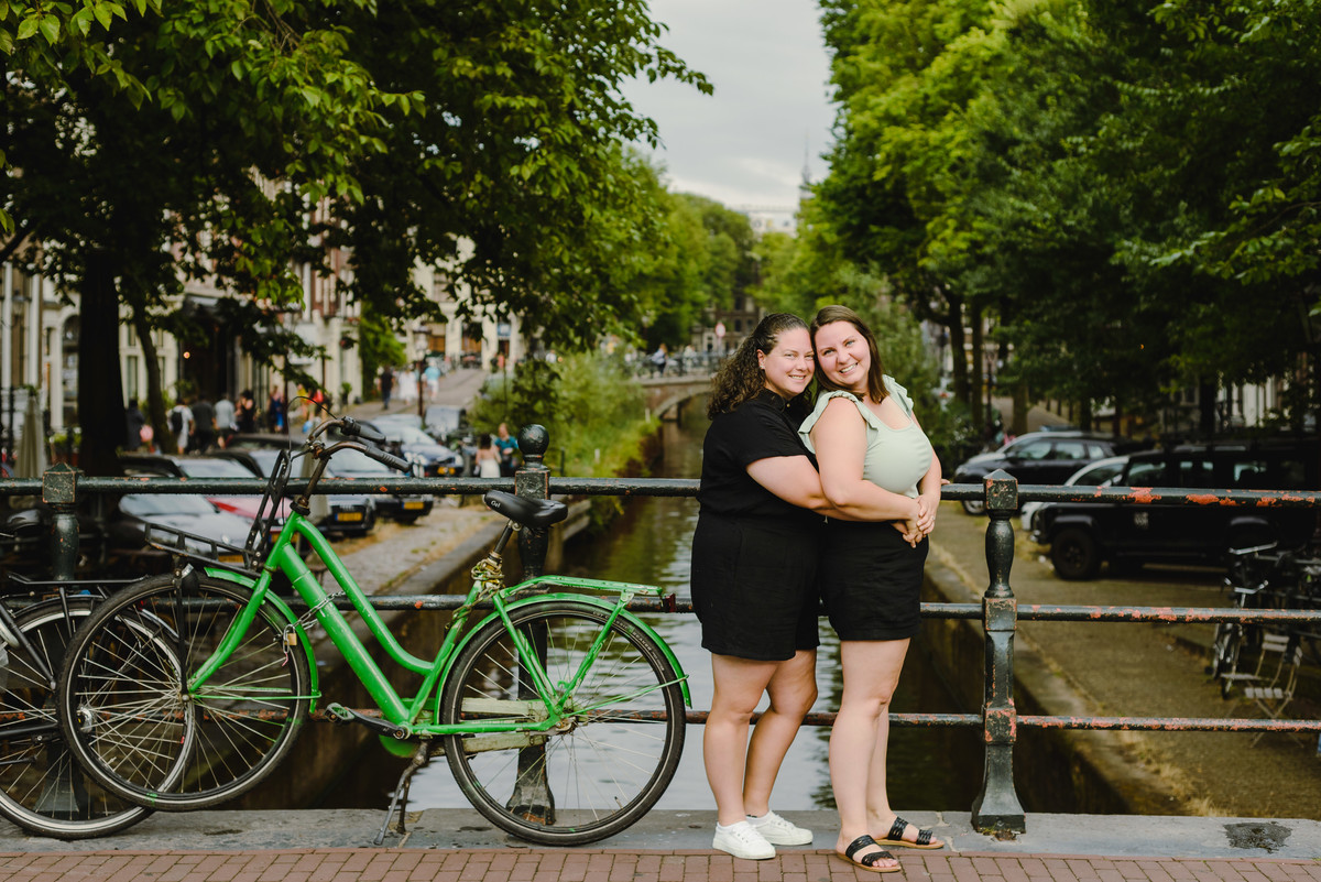 Same-sex couple posing with a bicycle beside an Amsterdam canal, summer photo session
