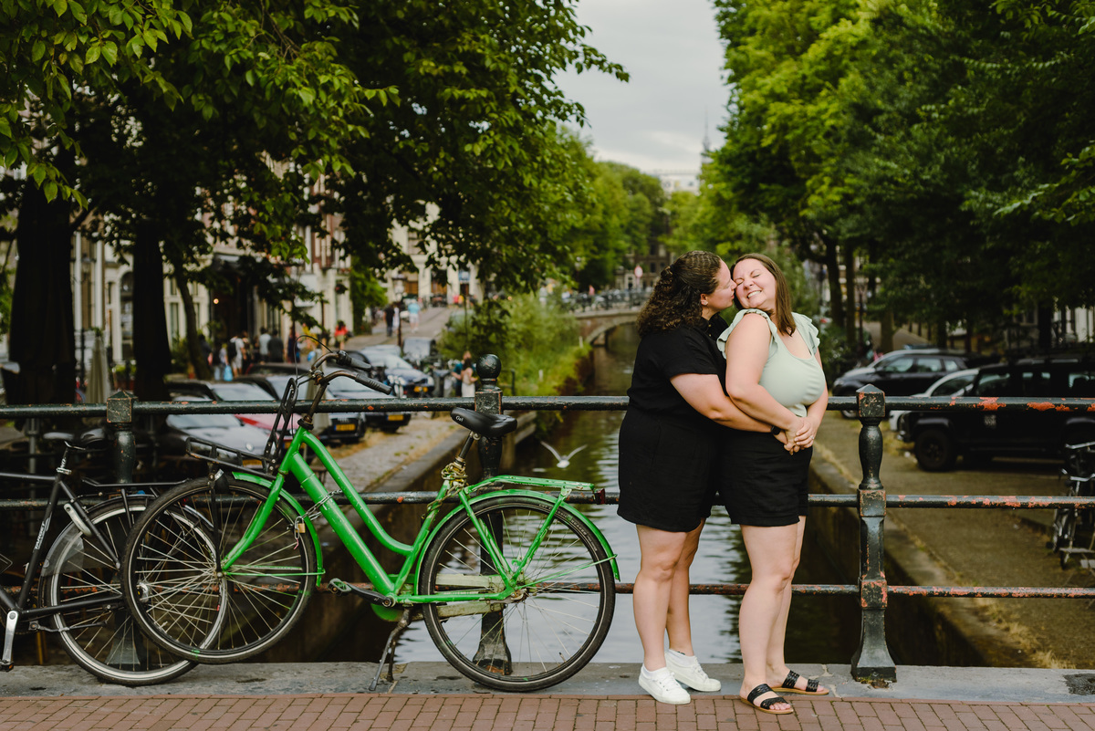 Same-sex couple posing with a bicycle beside an Amsterdam canal, summer photo session