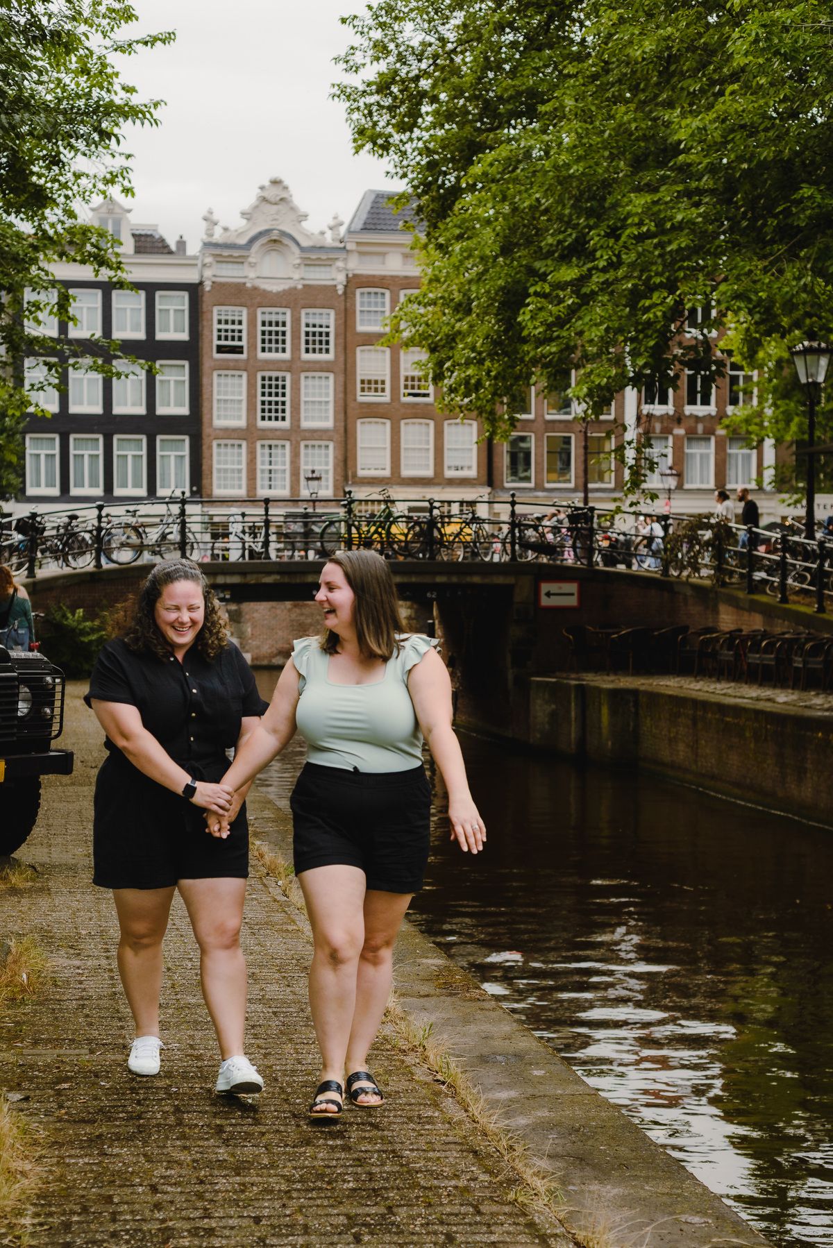 Romantic same-sex couple walking along an Amsterdam canal during a summer photo session