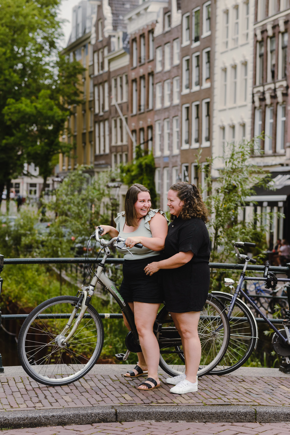 Same-sex couple posing with a bicycle beside an Amsterdam canal, summer photo session