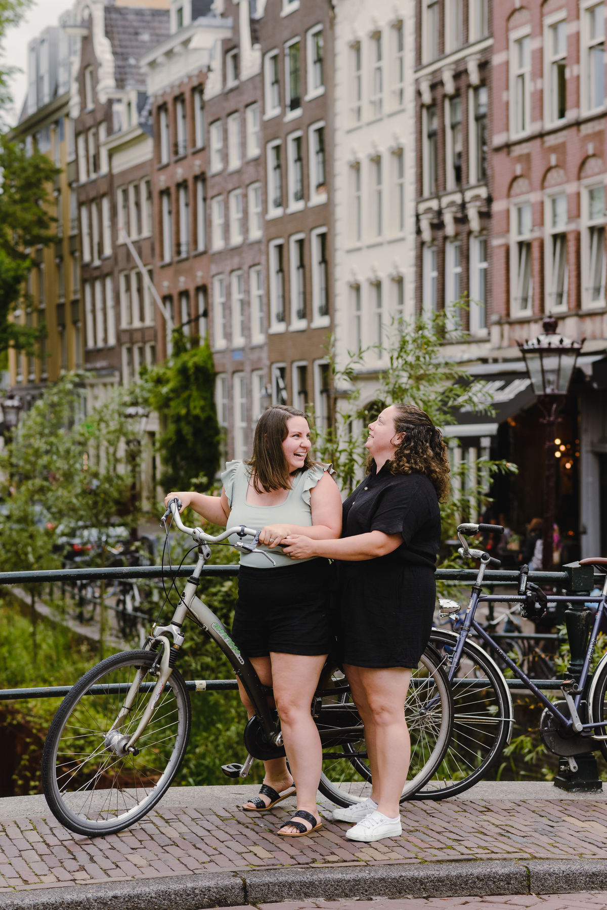 Same-sex couple posing with a bicycle beside an Amsterdam canal, summer photo session