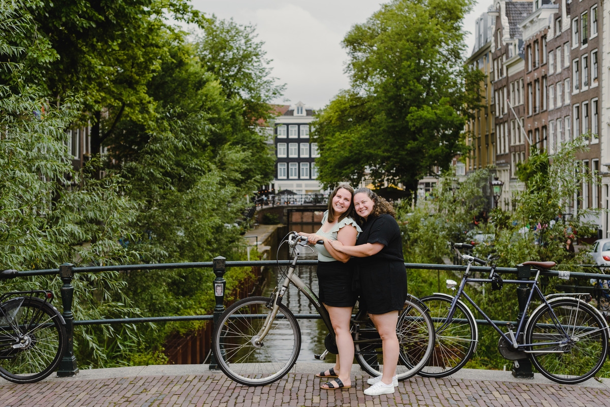 Same-sex couple posing with a bicycle beside an Amsterdam canal, summer photo session