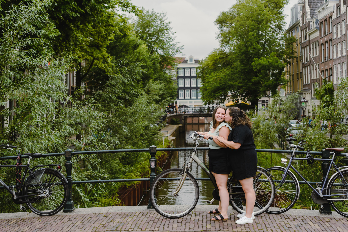 Same-sex couple posing with a bicycle beside an Amsterdam canal, summer photo session