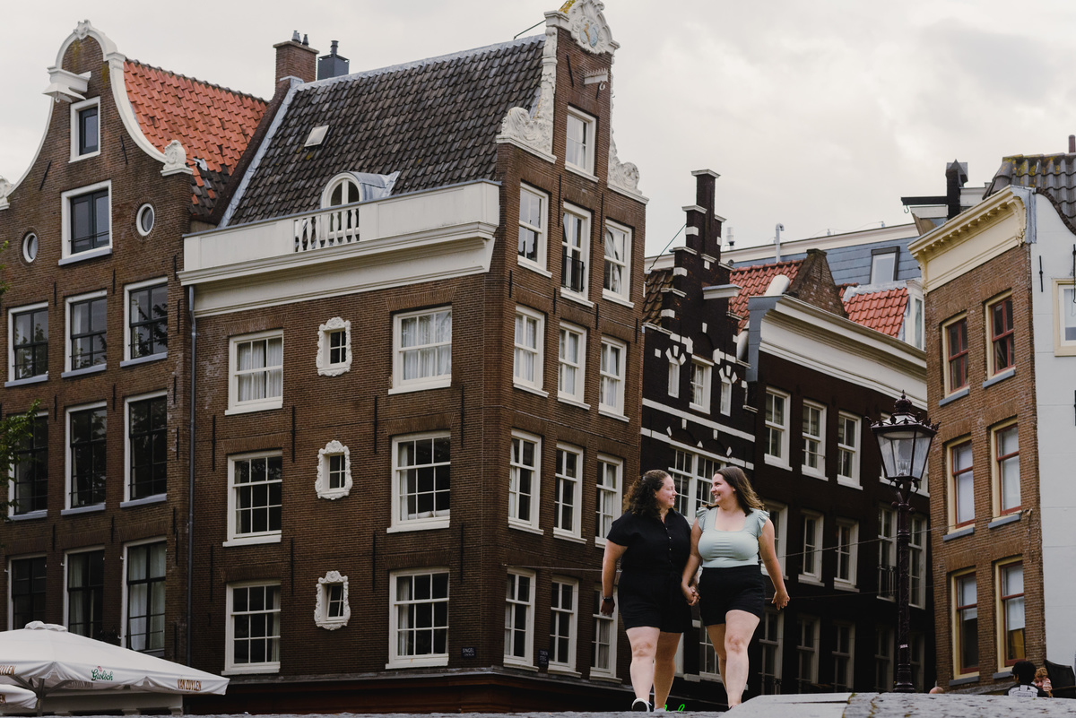Same-sex couple strolling through the Amsterdam canal belt with traditional houses in the background
