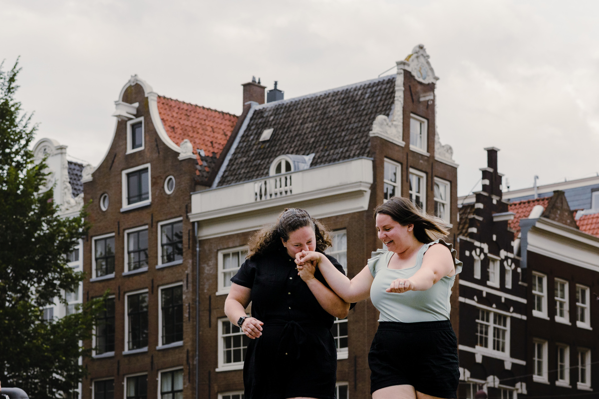 Same-sex couple strolling through the Amsterdam canal belt with traditional houses in the background