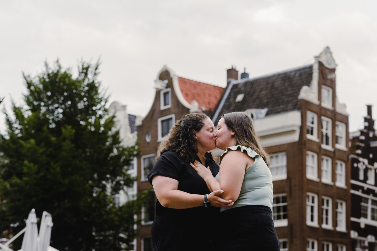 Same-sex couple strolling through the Amsterdam canal belt with traditional houses in the background