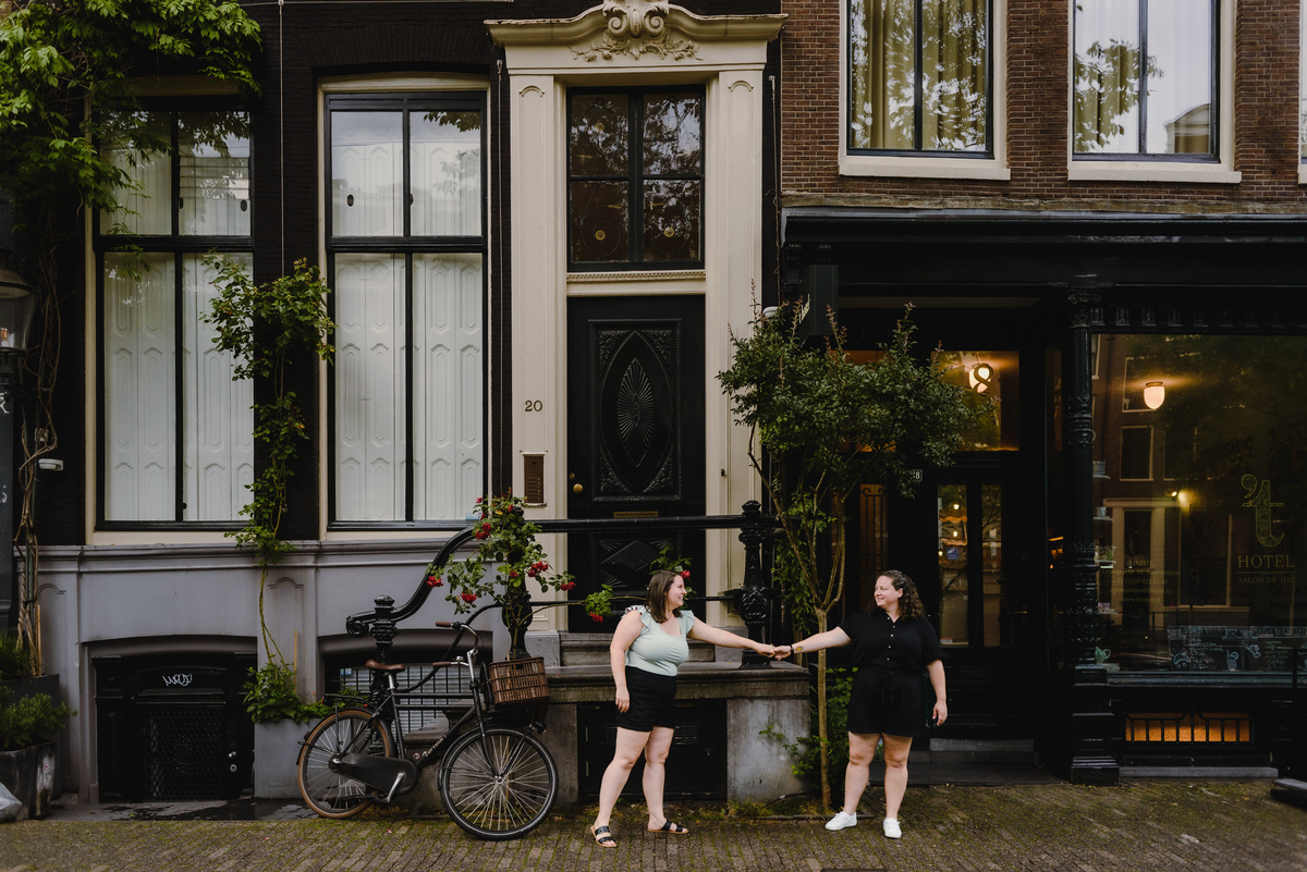 Same-sex couple strolling through the Amsterdam canal belt with traditional houses in the background