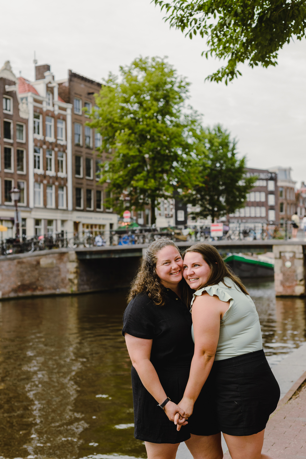 Same-sex couple posing together in Amsterdam with canals and historic buildings