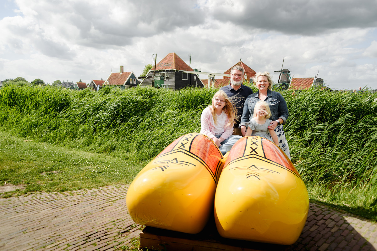 Family portrait on giant traditional dutch wooden shows at Zaanse Schans village with houses in the background