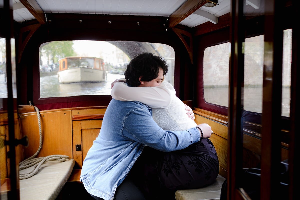 A couple share an embrace inside a historical boat in Amsterdam. You can see a boat behind them. They are happy; they are recently engaged. 