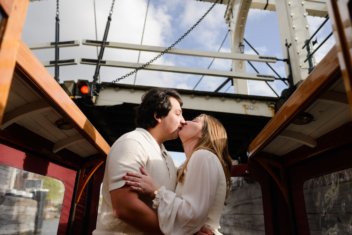 A couple is sharing a kiss while the boat navigates below the Skinny Bridge (Magere Brug) in Amsterdam. 