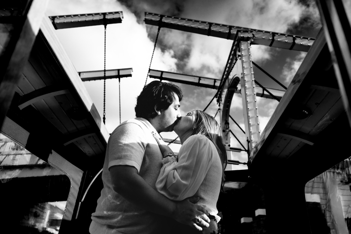 A black and white image of the couple sharing a kiss. They are newly engaged, and a kiss shared below the skinny bridge means that they are going to stay together forever. 