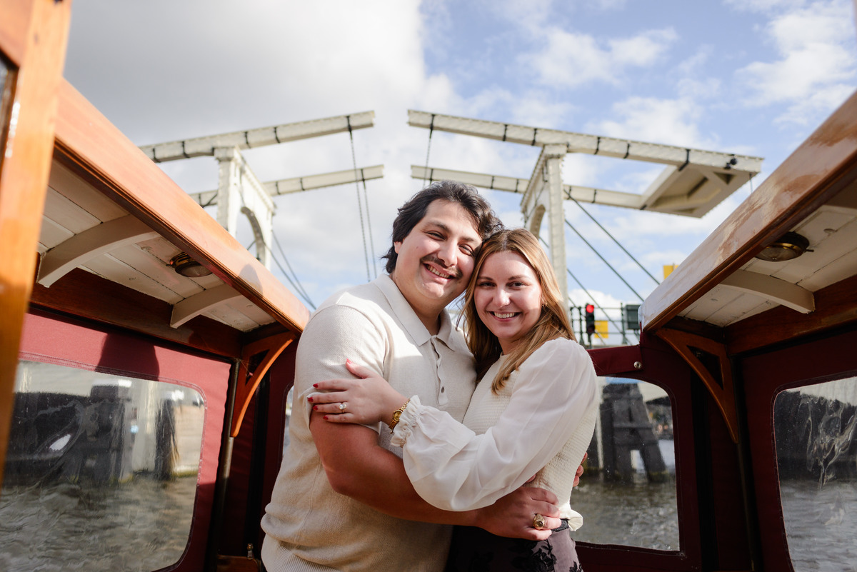 A couple smiles after their engagement proposal and passing below the Skinny Bridge while navigating the canals of Amsterdam 