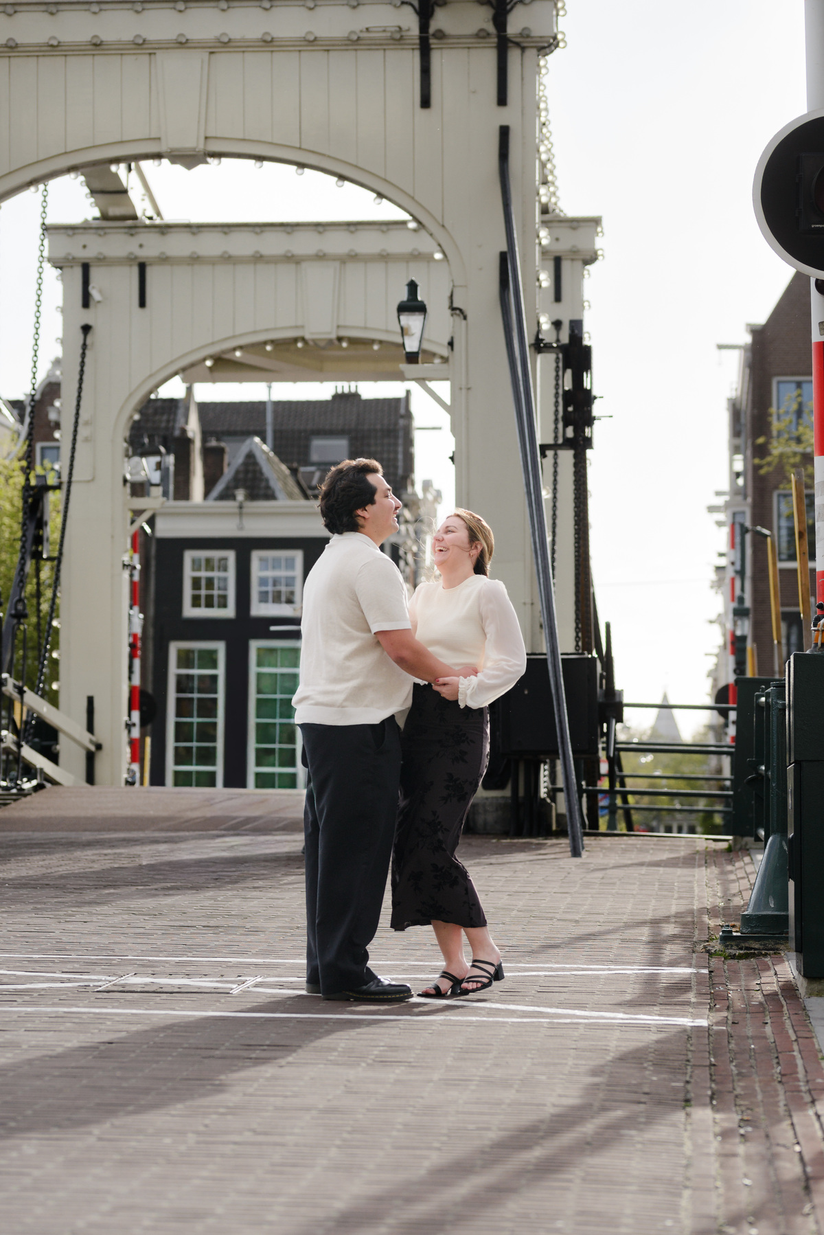After an engagement proposal in Amsterdam, they walk on the streets in Amsterdam. A young couple is walking the streets in Amsterdam. They are crossing the skinny bridge. 