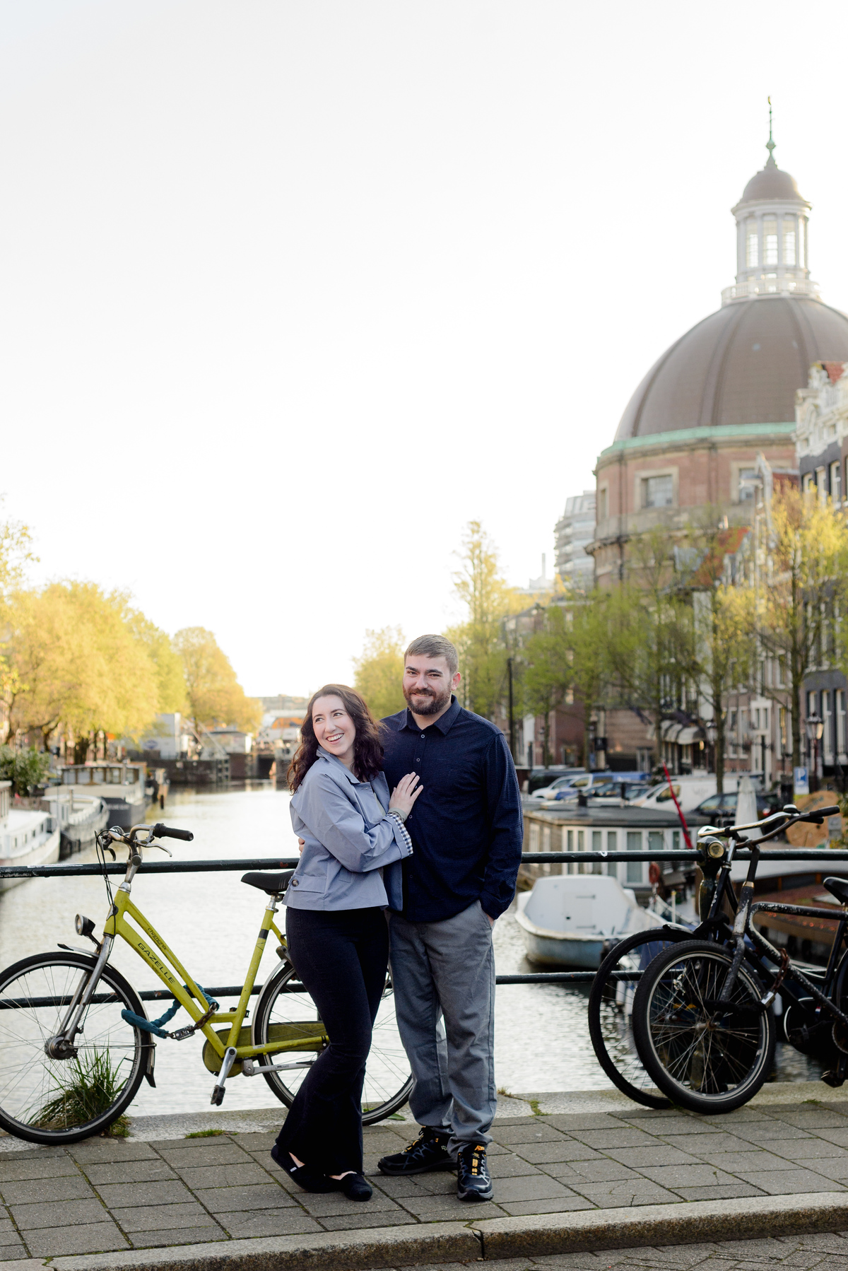 Couple celebrating anniversary in Amsterdam, making a photo shoot on the canals with the view of the Singel behind them 