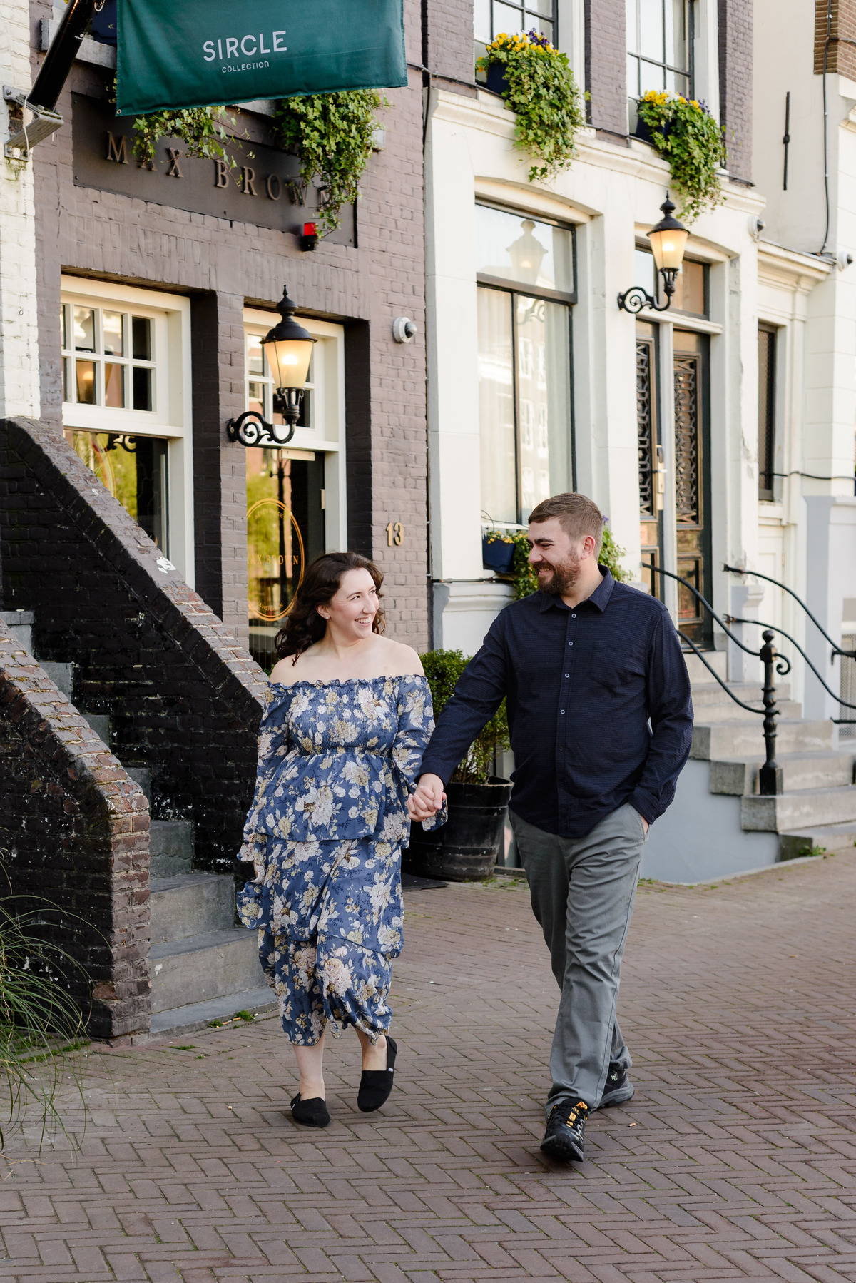 During a photo session in Amsterdam in the canal belt, a couple walks along the streets with historical houses in the background. 