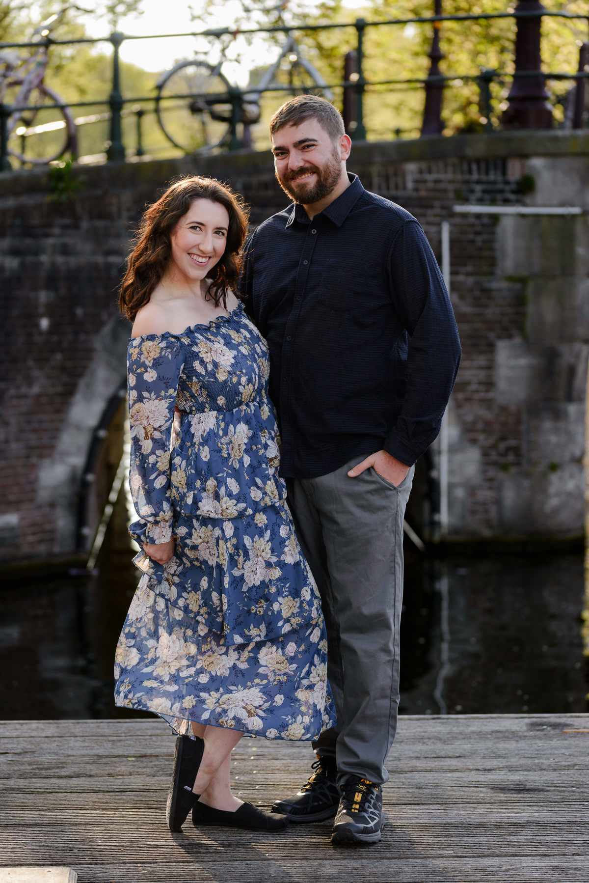 Happy couple celebrating anniversary is smiling at a camera during a photo session in Amsterdam. The canal bell is one of the best locations to photograph in Amsterdam. 