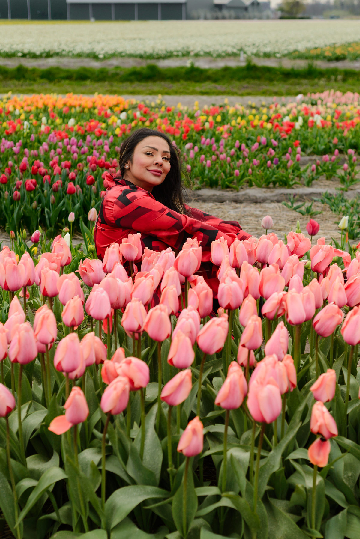 Female solo traveler smiling in a photo session with tulips in the foreground and background, surrounded by tulips, in Tulip Experience Amsterdam during Tulip Season 2026. 