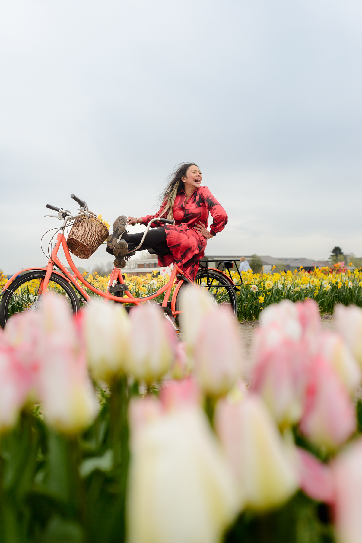 Female solo traveler, extremely happy and on a bike, surrounded by tulips. A Tulip Experience Amsterdam during Tulip Season 2026. This is during a tulip photo session 