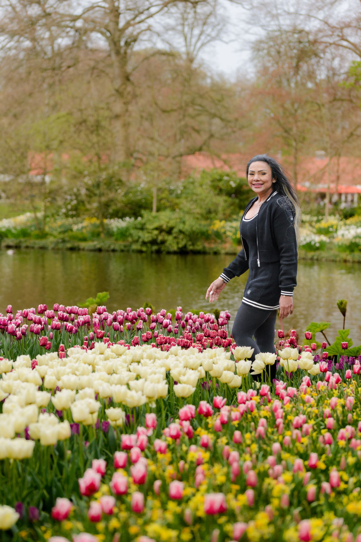 Solo traveler walking at Keukenhof Gardens with a river behind her and tulips surrounding her. This is a photo session taken during Tulip Season 2026. 