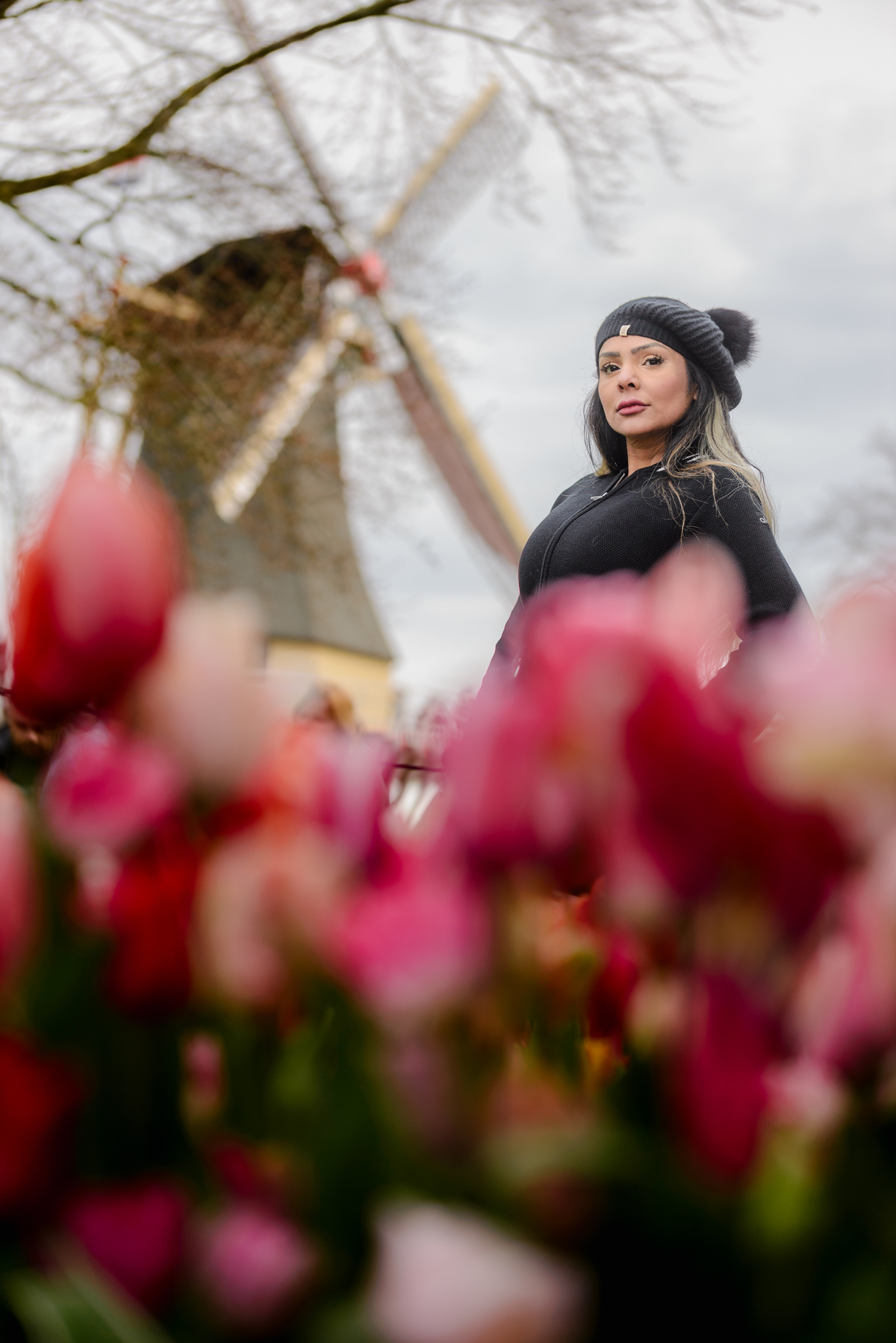 Female solo traveler posing during a photo session in Keukenhof Gardens, with tulips in front of her and an iconic windmill behind her. 