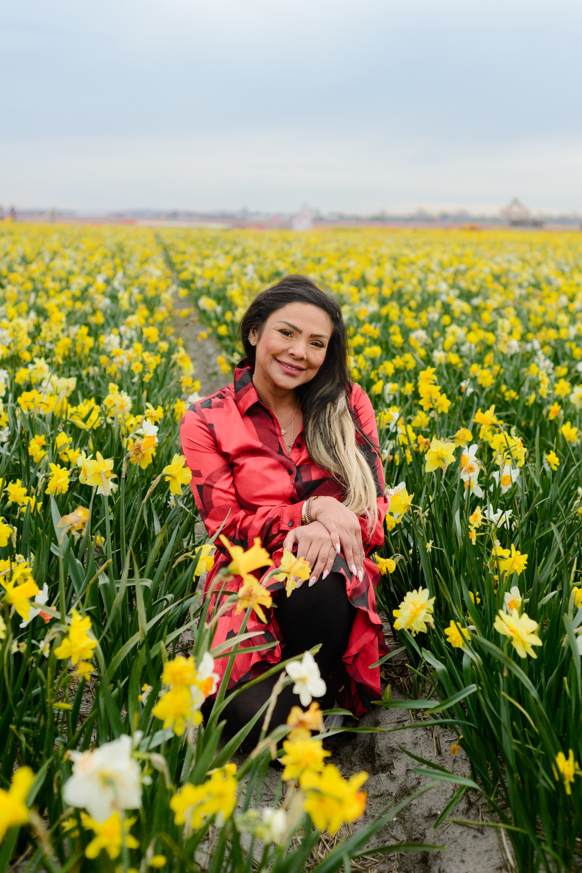 Female solo traveller smiling, sitting in a daffodil field in Tulip Experience Amsterdam during Tulip Season 2026. 