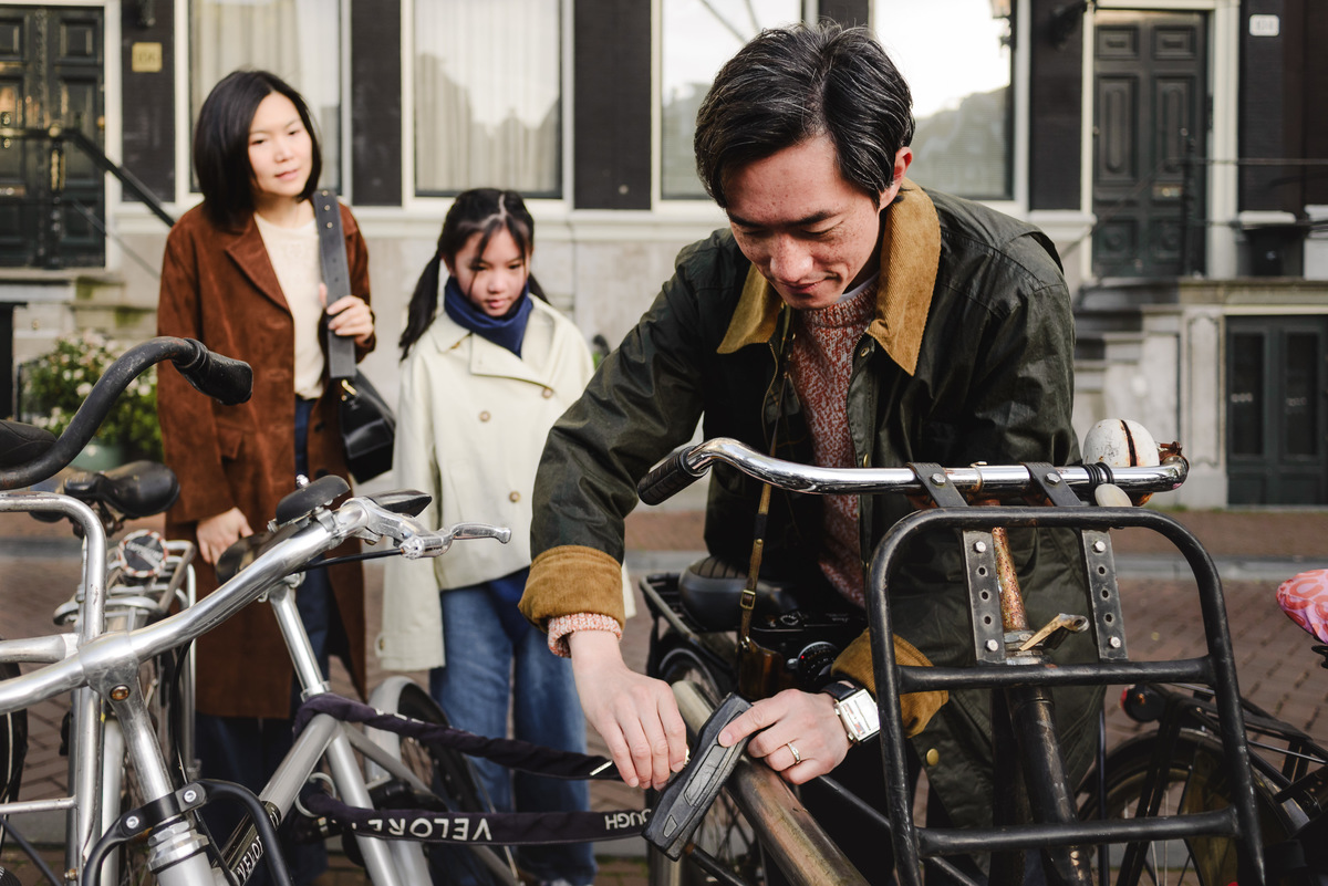Father unlocking a bicycle while his family watches during a morning in Amsterdam