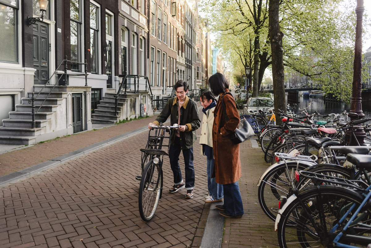 Father riding a bicycle along an Amsterdam canal while his family watches