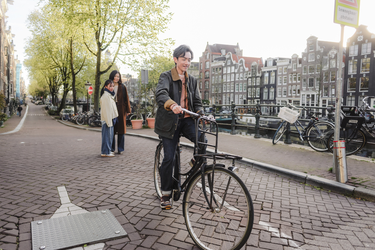 Father riding a bicycle along an Amsterdam canal while his family watches