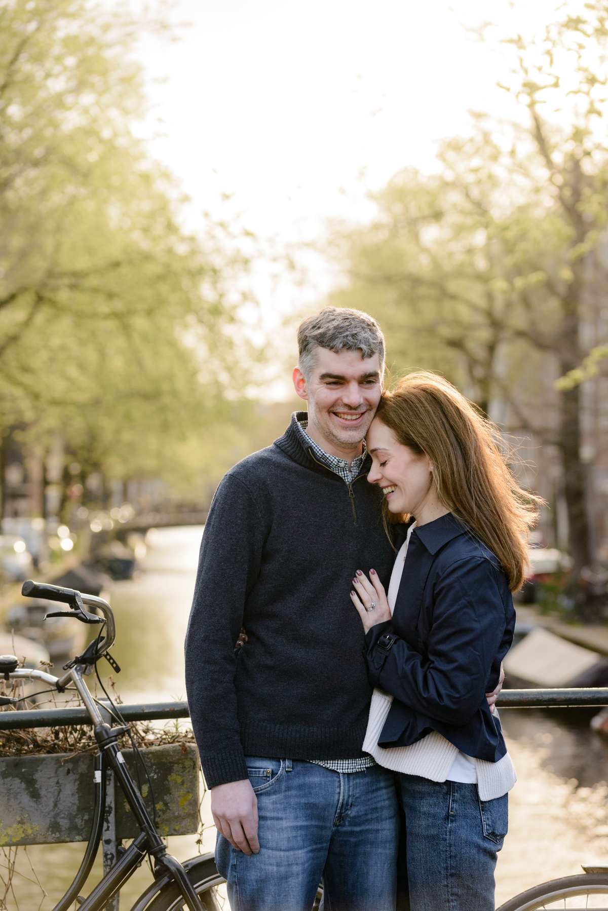 Parents sharing a quiet moment beside an Amsterdam canal at sunset during a family trip to the Netherlands