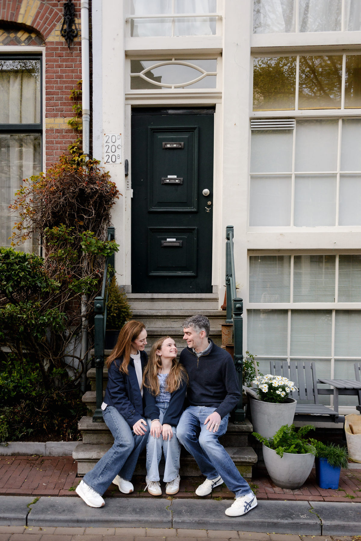 Family sitting together on the steps of a traditional Amsterdam canal house during their annual family photo tradition