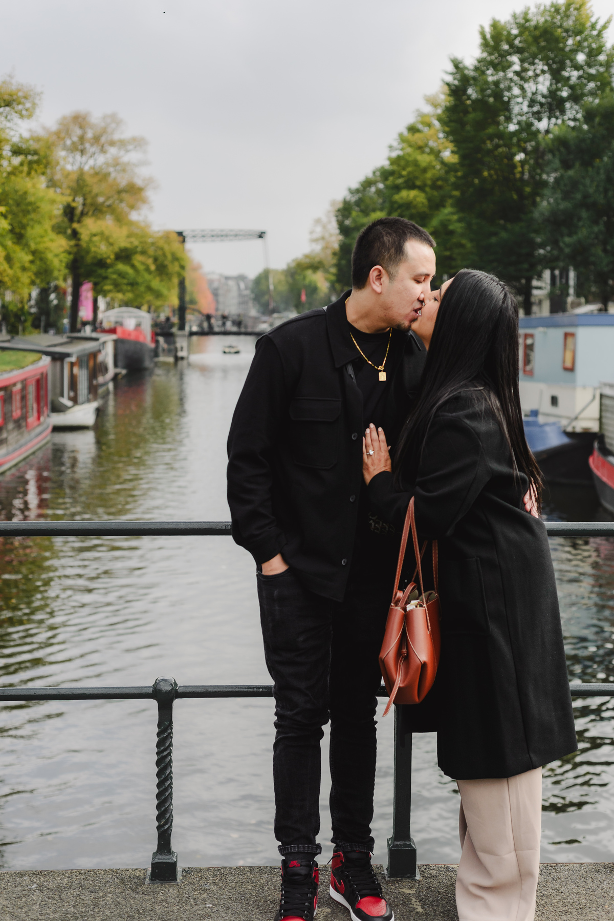 Recently engaged couple smiling together on Dommersbrug with Brouwersgracht canal and historic Amsterdam houses in the background.