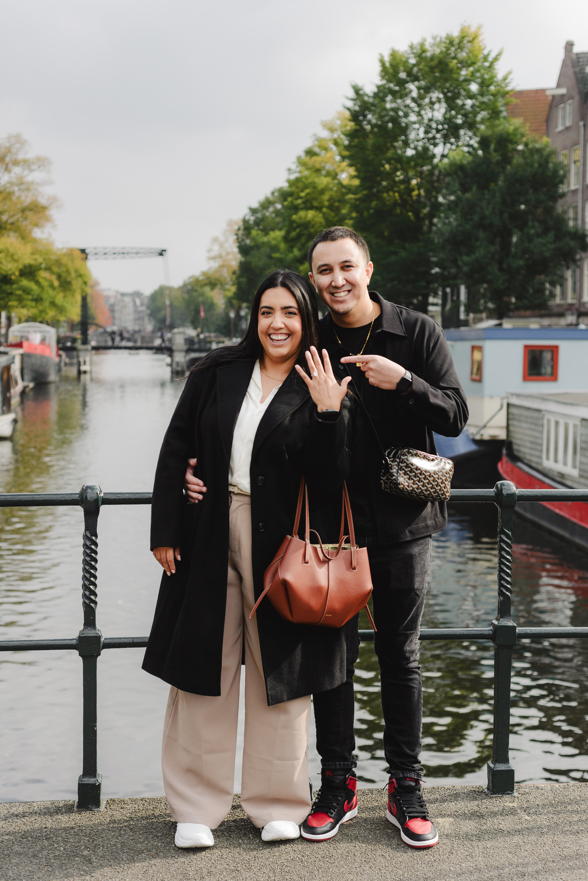 Couple standing on a canal bridge in Amsterdam moments after a surprise proposal while admiring the engagement ring.