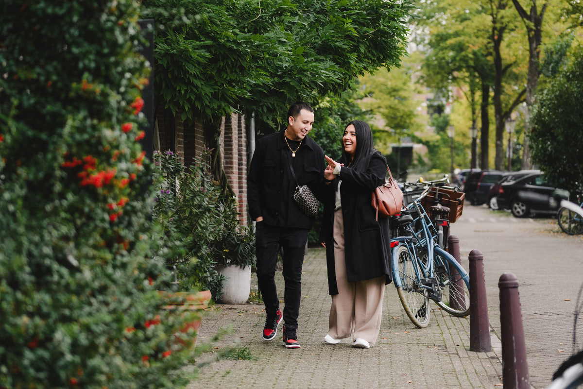 Engaged couple walking hand in hand through a quiet Jordaan street lined with bicycles, trees, and traditional Amsterdam houses.