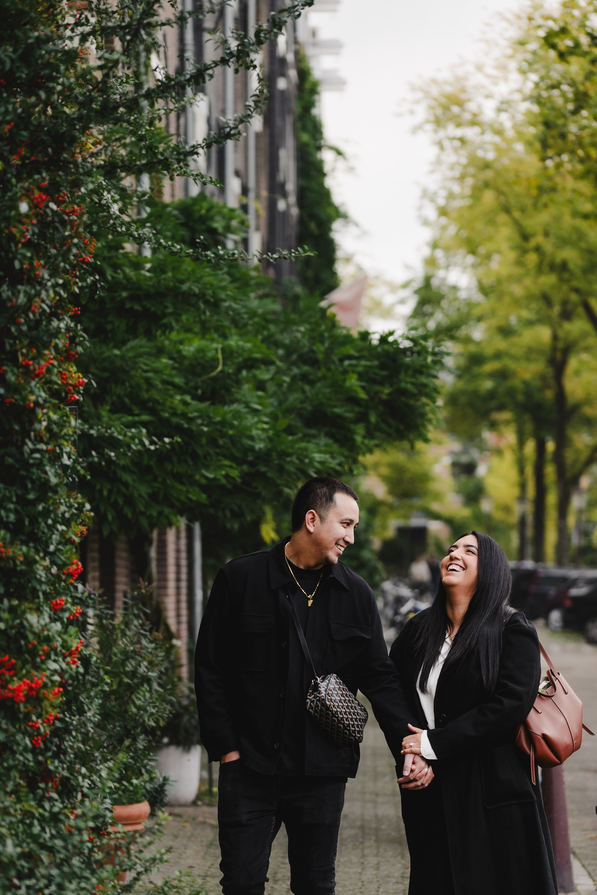 Engaged couple walking hand in hand through a quiet Jordaan street lined with bicycles, trees, and traditional Amsterdam houses.
