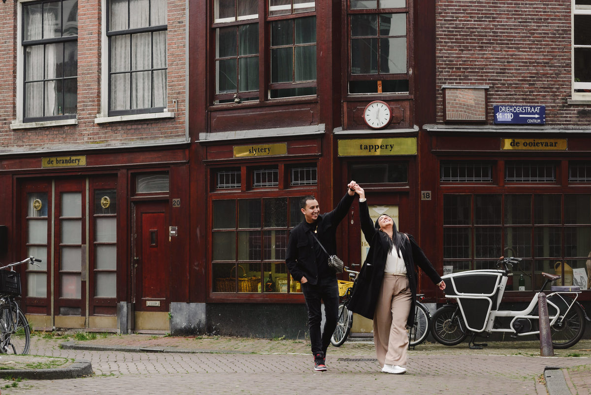 Couple laughing together beside an ivy-covered brick building during an engagement photo session in Jordaan, Amsterdam.