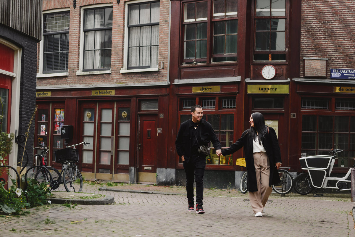 Couple laughing together beside an ivy-covered brick building during an engagement photo session in Jordaan, Amsterdam.