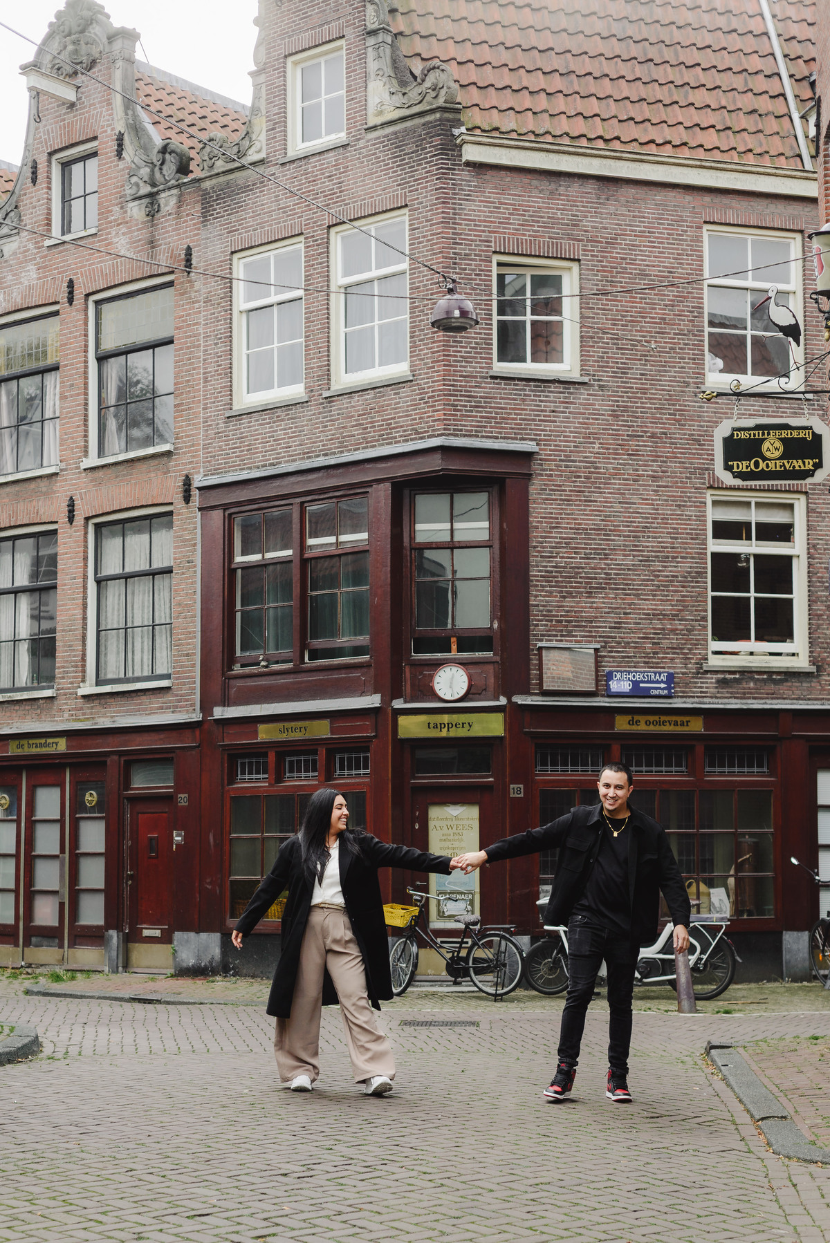 Couple laughing together beside an ivy-covered brick building during an engagement photo session in Jordaan, Amsterdam.