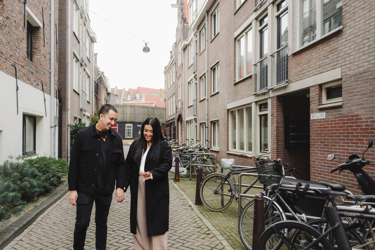 Couple laughing together beside an ivy-covered brick building during an engagement photo session in Jordaan, Amsterdam.