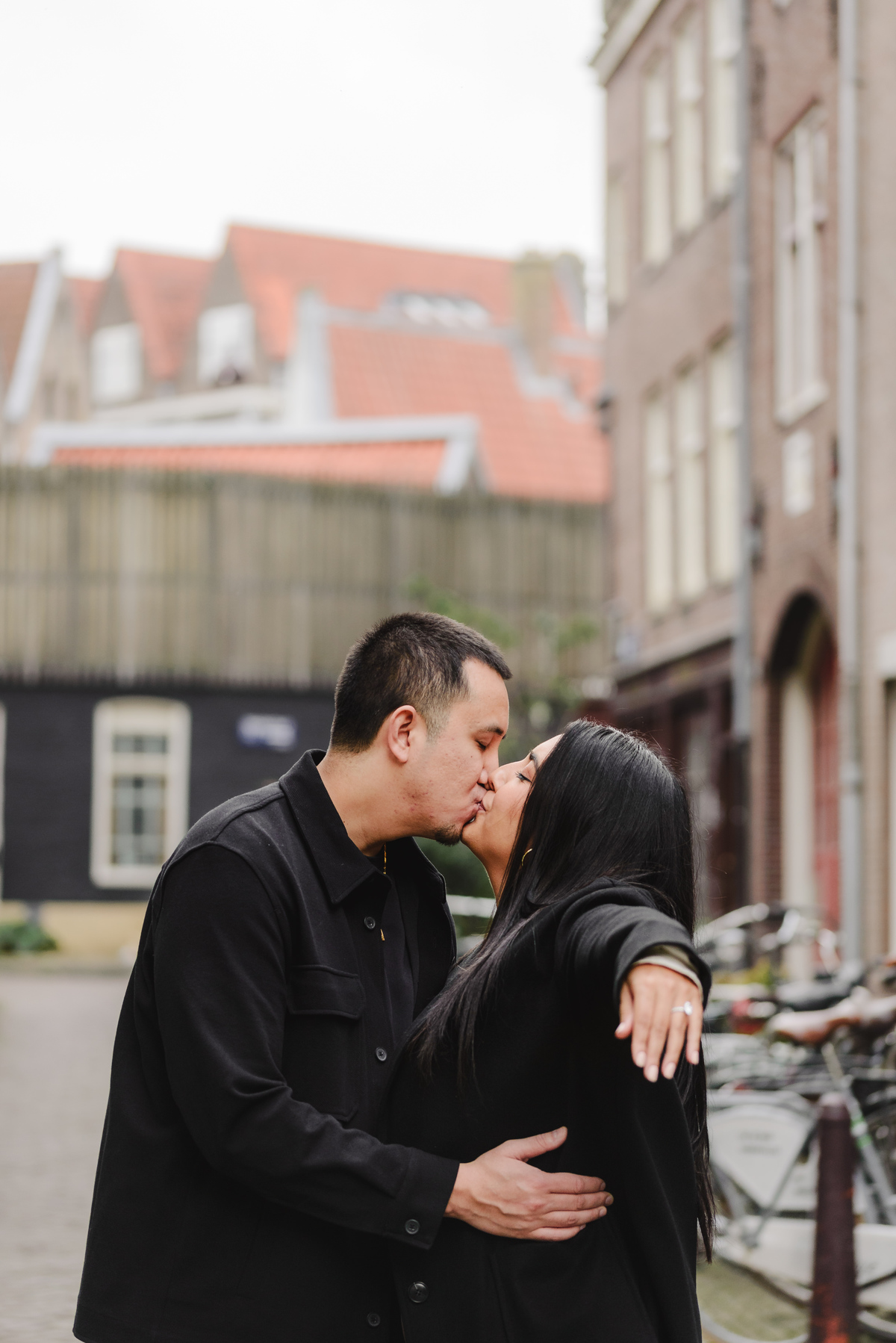 Couple laughing together beside an ivy-covered brick building during an engagement photo session in Jordaan, Amsterdam.